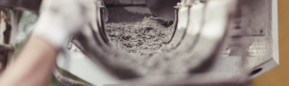 Close-up of concrete being poured from a mixer truck at a construction site with a worker's hand visible.