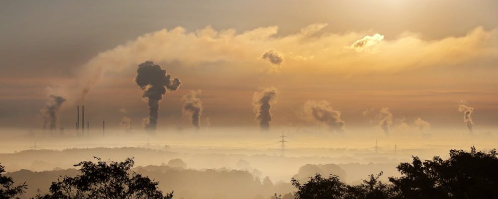 Smoke rising from factory chimneys at sunrise, symbolizing pollution and environmental impact.