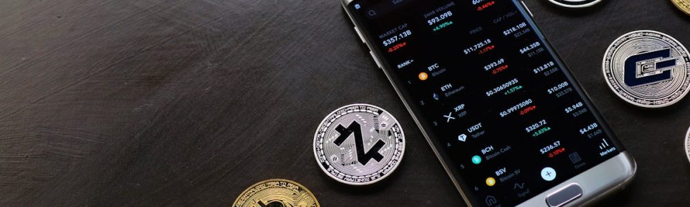 A collection of cryptocurrency coins and a smartphone displaying a digital trading platform.