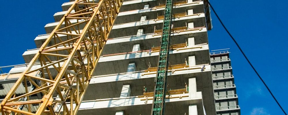 Low-angle view of skyscraper under construction with crane, clear blue sky.