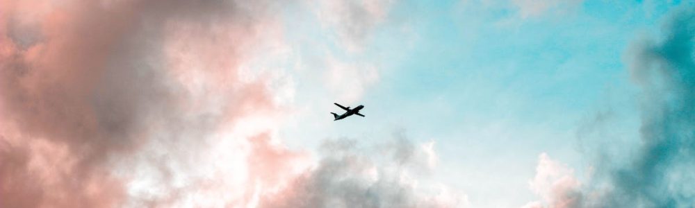 A plane flying through a colorful sky with pink and blue clouds, capturing the essence of travel.