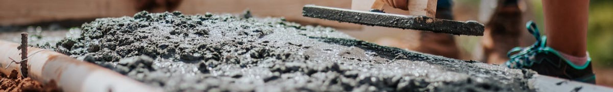 Construction workers leveling fresh cement on a sunny day at an outdoor site.