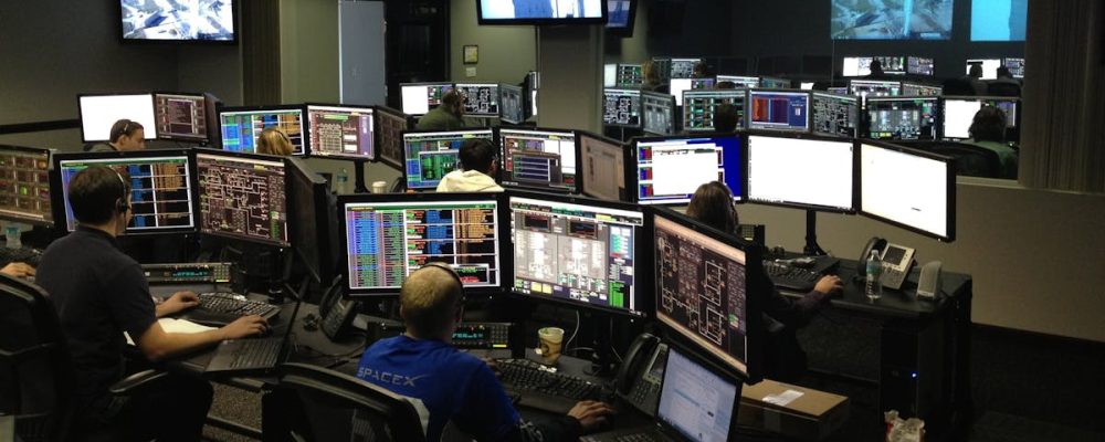 A bustling control room with people working on multiple computer monitors.