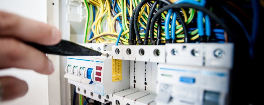 Hand of electrician working on a circuit breaker panel with colorful wires, ensuring safe electrical connections.