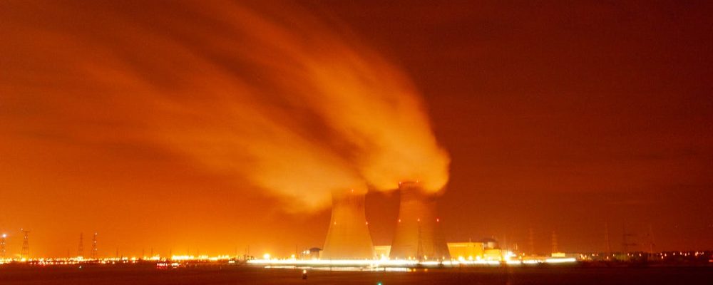 A dramatic view of cooling towers emitting steam against an orange night sky, showcasing industrial energy production.