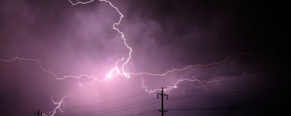 Stunning lightning bolts illuminate a stormy night sky over silhouetted power lines.