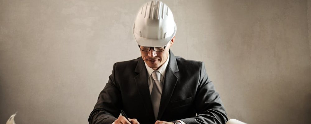 Engineer in a suit drafting architectural plans at a desk indoors.