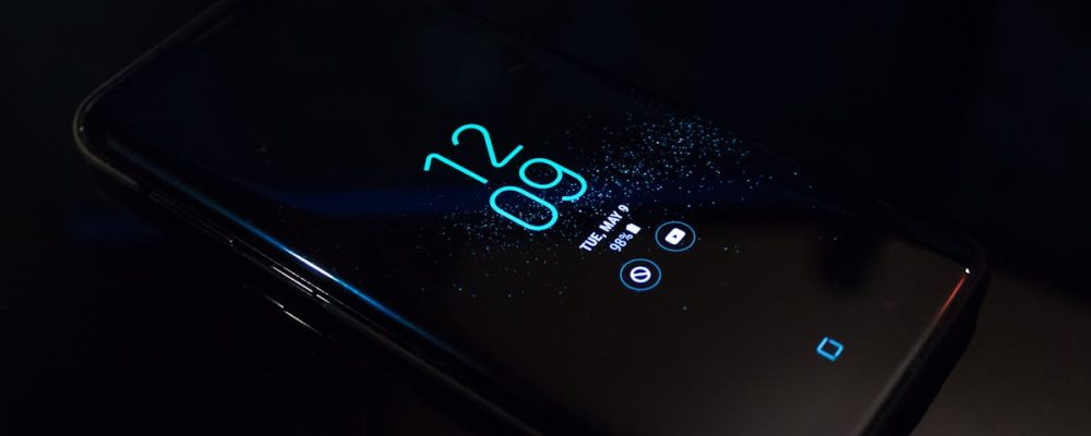 Close-up of a smartphone in the dark displaying digital clock and notifications.