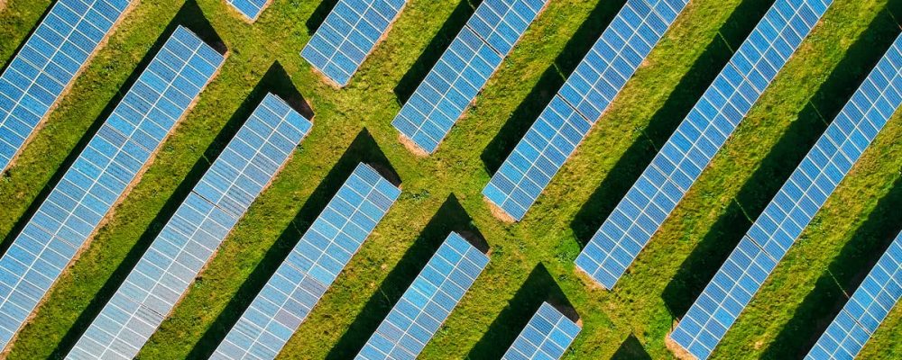 High-angle aerial shot of solar panels in a lush green field, located in Rockbeare, UK.