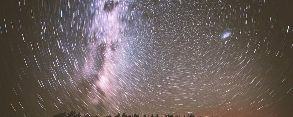 A captivating long-exposure shot of star trails and the Milky Way above silhouetted trees at night.