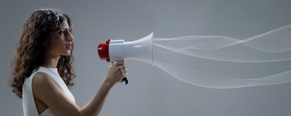 Woman using a megaphone emitting sound waves on a gray background.