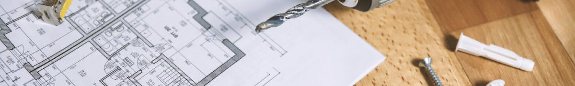 Close-up of construction blueprint with tools like drill and screws on a wooden table.