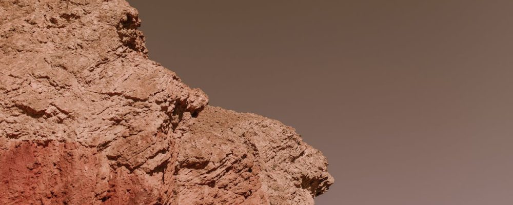 A lone astronaut in a space suit exploring rocky, Mars-like desert terrain.