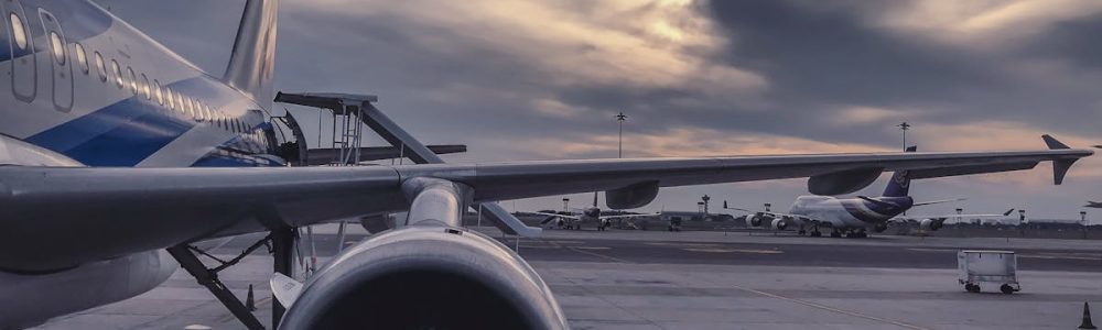 A passenger airplane is parked on the tarmac at sunset, with another aircraft in the background.