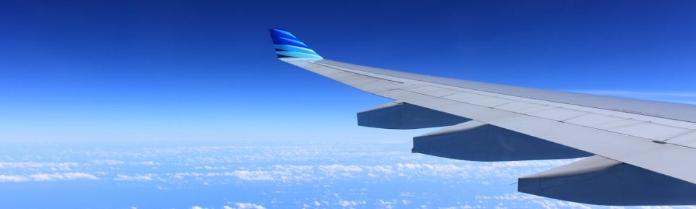 Scenic view of an airplane wing flying high above the clouds on a clear day.